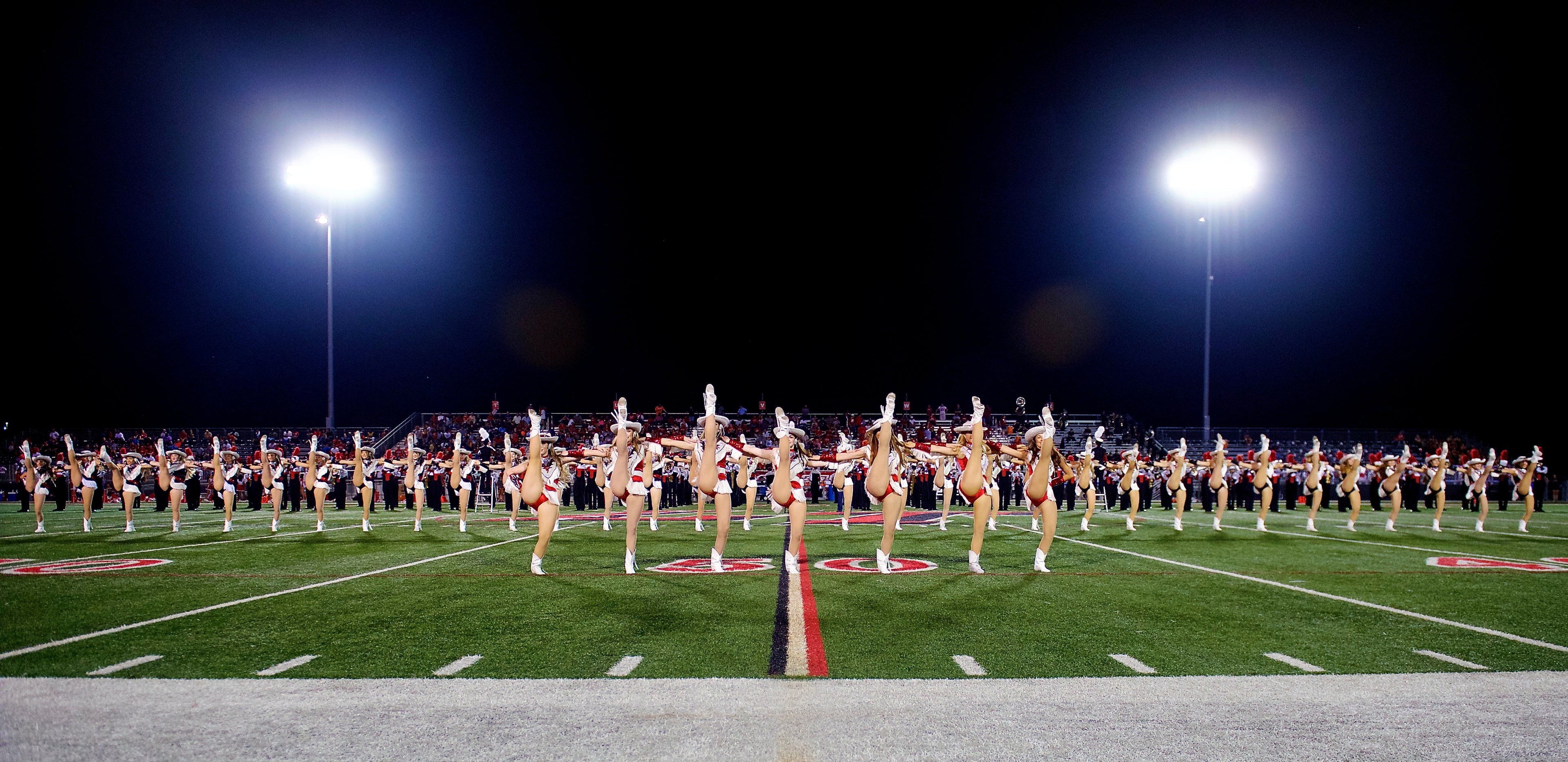 A high school drill team doing high kicks on a football field.