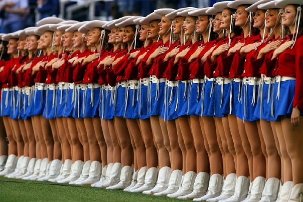 A line of young women in drill team outfits with their hands over their hearts.